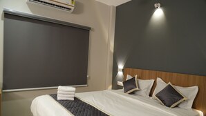 Un lit bien fait, avec une tête de lit matelassée, un climatiseur fixé au mur et une lampe de chevet.