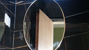 Une salle de bain avec un miroir rond, un lavabo et une porte en bois, le tout se reflétant dans le miroir.