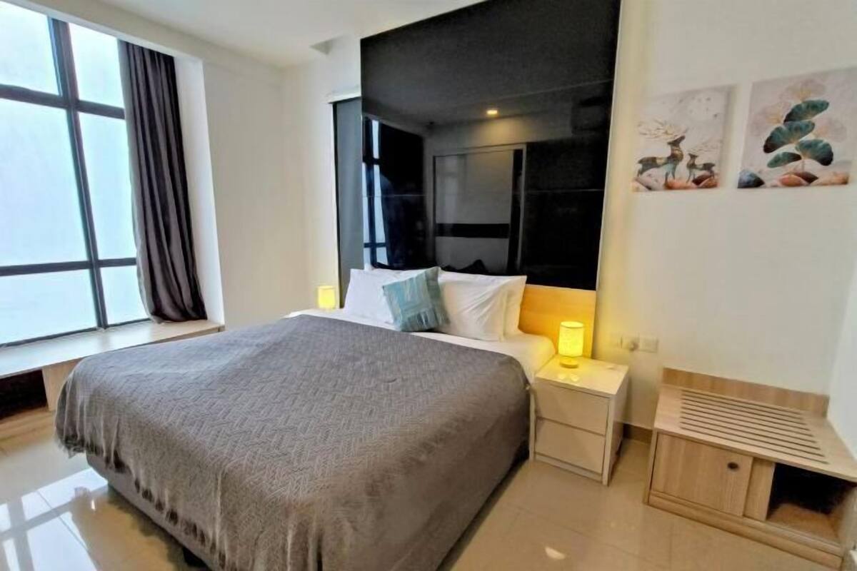 A modern hotel room with a large bed, bedside tables, a window with curtains, and artwork on the wall.