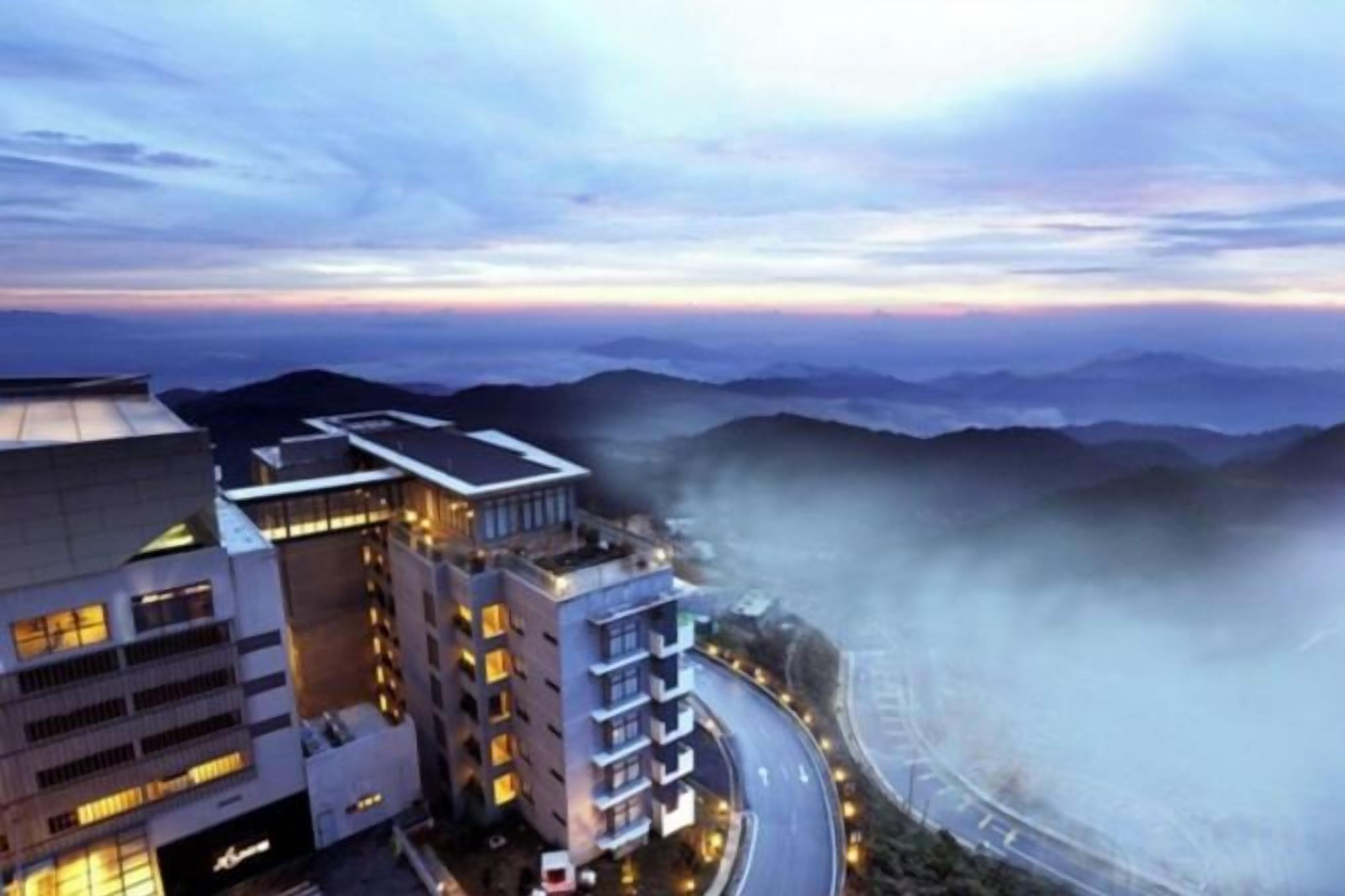 A hotel with multiple floors, a curved road, and a mountainous backdrop.