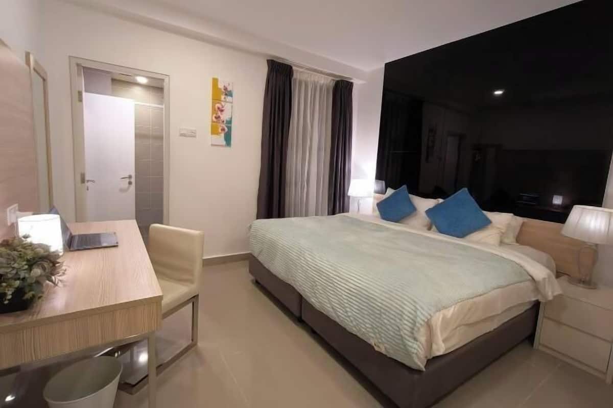 A hotel room with a bed, bedside table, chair, desk, and a door leading to a bathroom.