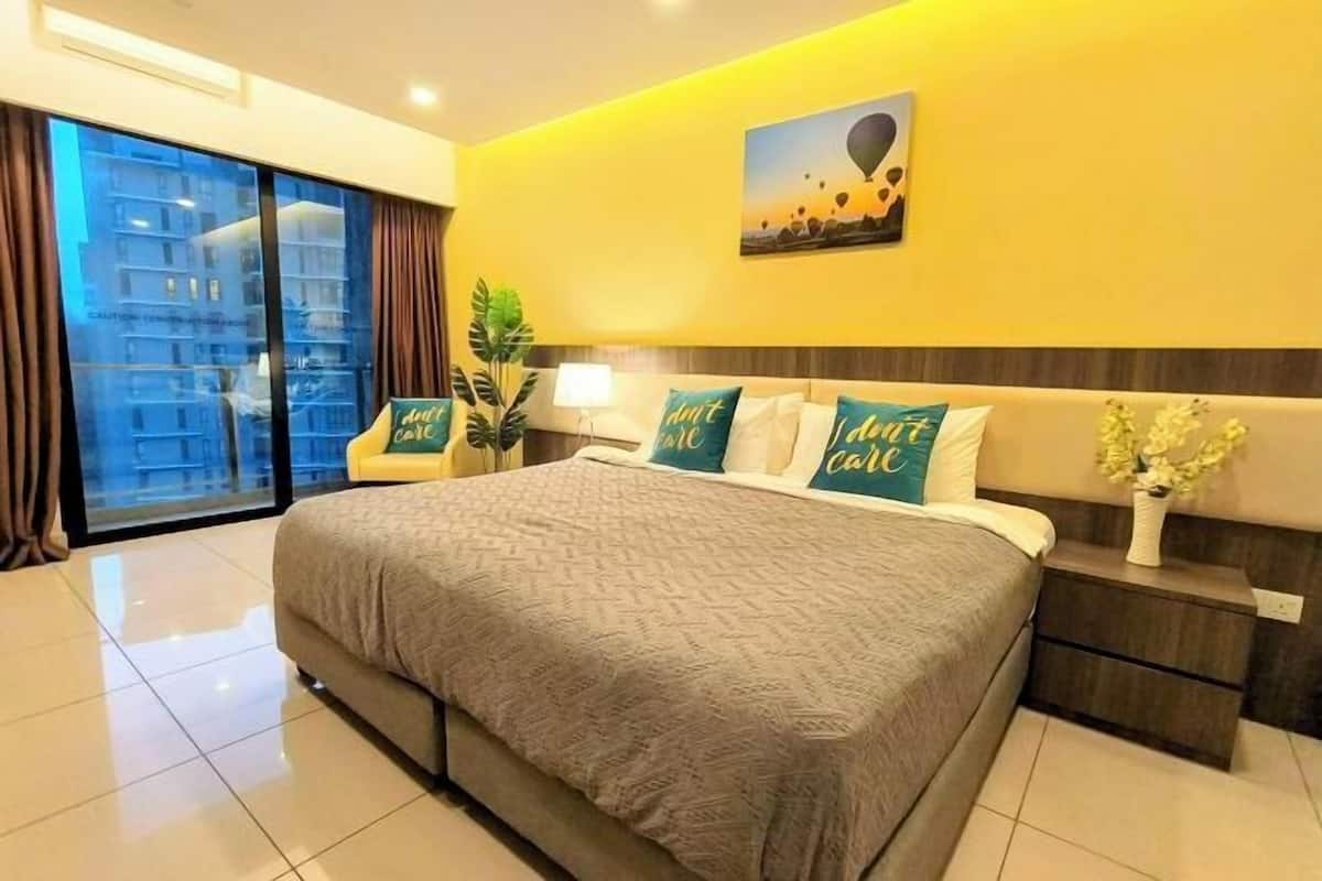 A hotel bedroom with a large bed, a nightstand, a lamp, and a view of a building through a glass door.