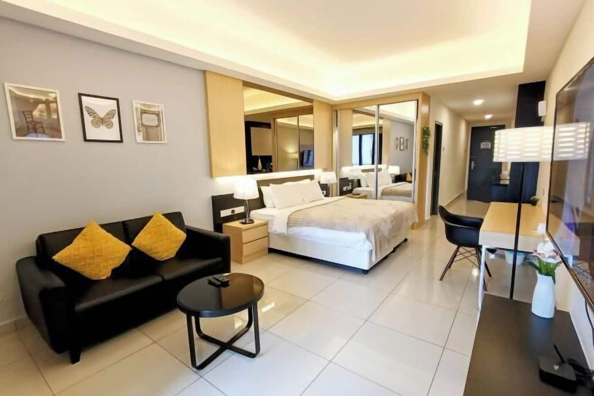 A modern hotel room with a bed, a black sofa with yellow cushions, a small table, a desk, and a mirror.