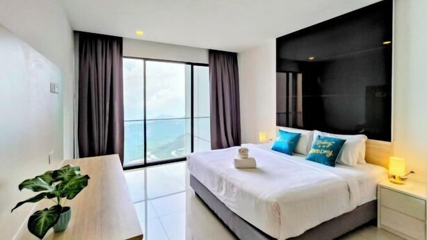 A modern hotel room with a large bed, a nightstand, a potted plant, and a view of the city through large windows. - Emerald Homes Cozy Homestay @ Genting Highlands (Genting Highlands)