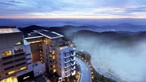 A modern hotel with multiple floors, a curved driveway, and a view of distant mountains. - Emerald Homes Cozy Homestay @ Genting Highlands (Genting Highlands)