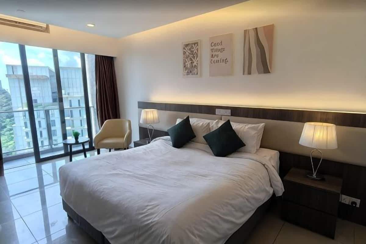 A modern hotel room with a large bed, bedside tables, a chair, and a view of the city.