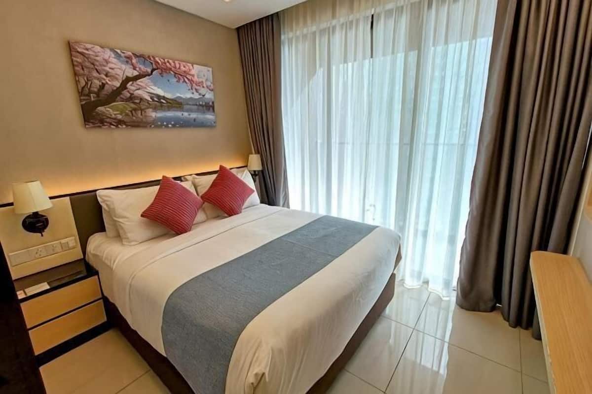 A hotel room with a bed, a nightstand, a lamp, a painting, and a view of the outdoors.