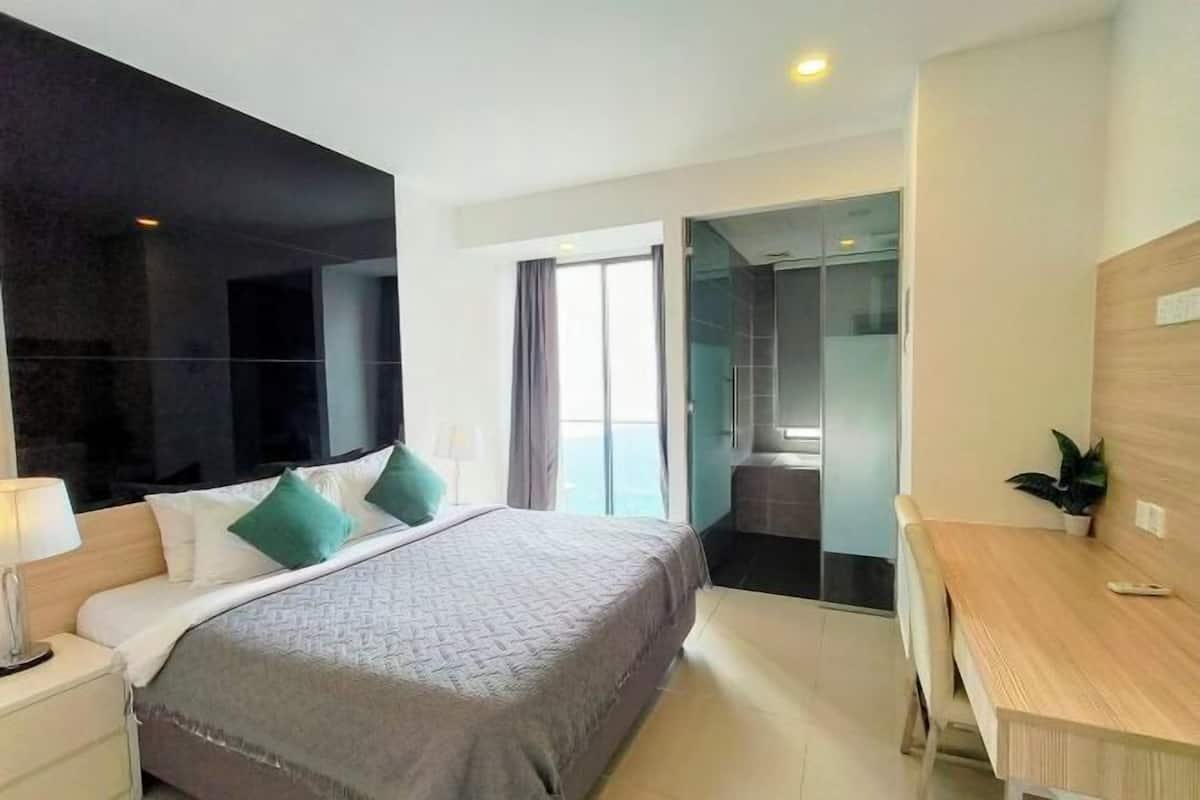 A modern hotel room with a large bed, a desk, and a glass-enclosed shower area.