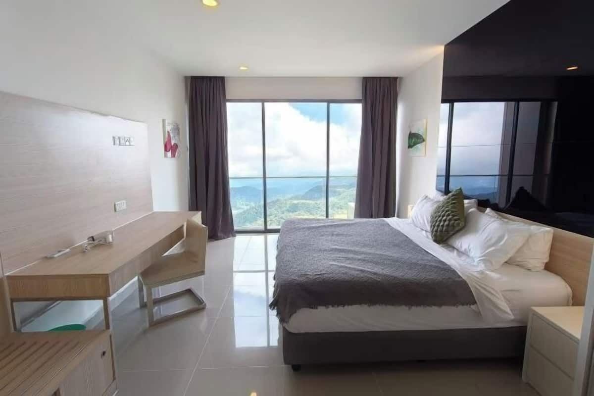 A modern hotel room with a large bed, a desk, and a view of the mountains.