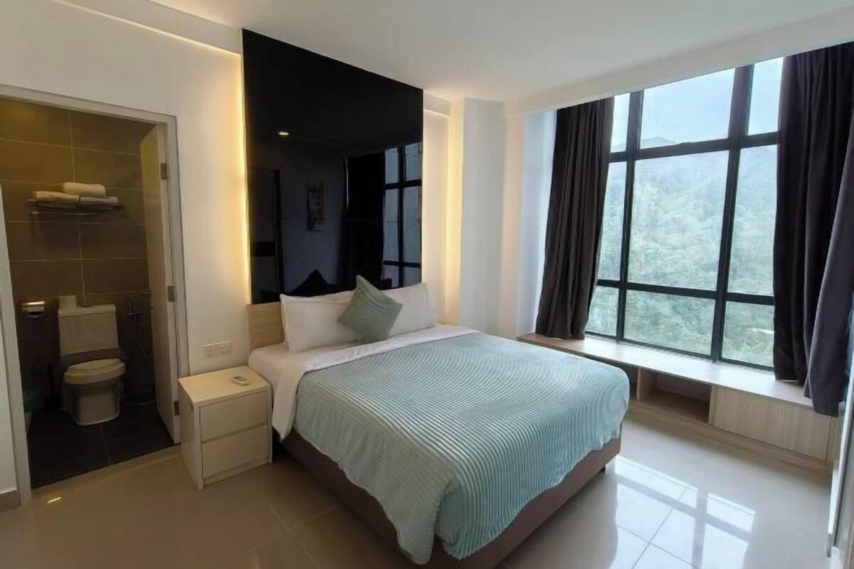 A modern bedroom with a large bed, a bedside table, a window with curtains, and a view of the outdoors.