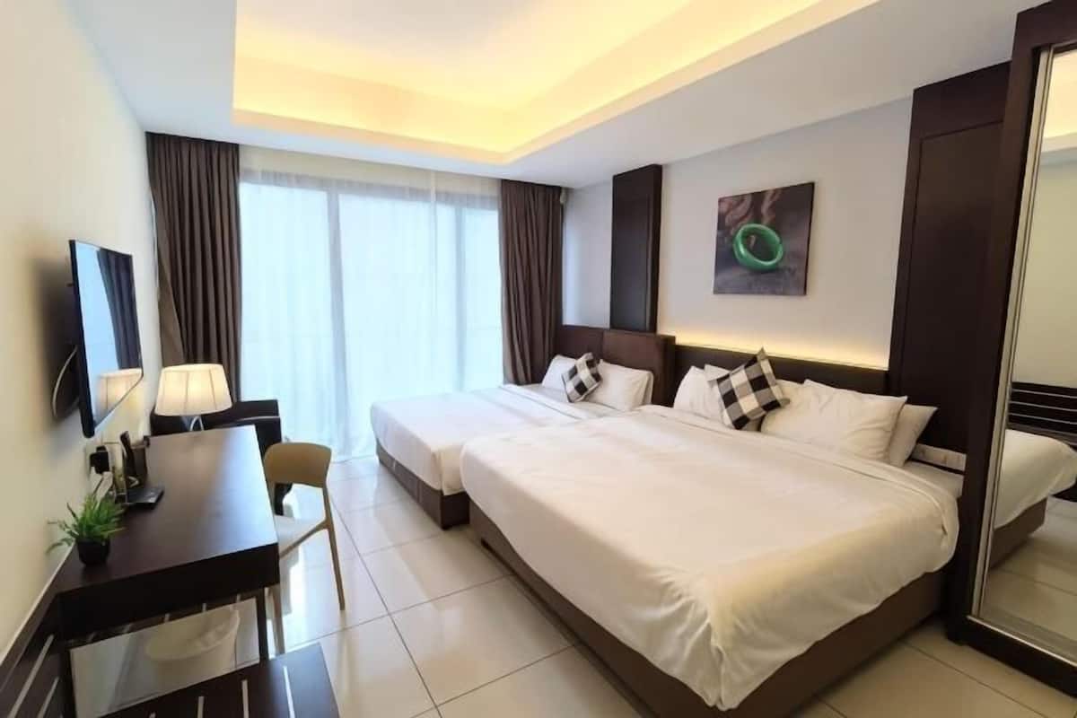 A hotel room with two beds, a desk, a chair, a TV, and a window with curtains.
