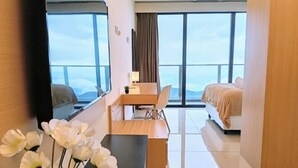 A modern hotel room with a large bed, a desk with a chair, and a view of the city through large windows. - Emerald Homes Cozy Homestay @ Genting Highlands (Genting Highlands)