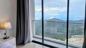 A hotel room with a large window, a bed, a nightstand, and a lamp. - Emerald Homes Cozy Homestay @ Genting Highlands (Genting Highlands)