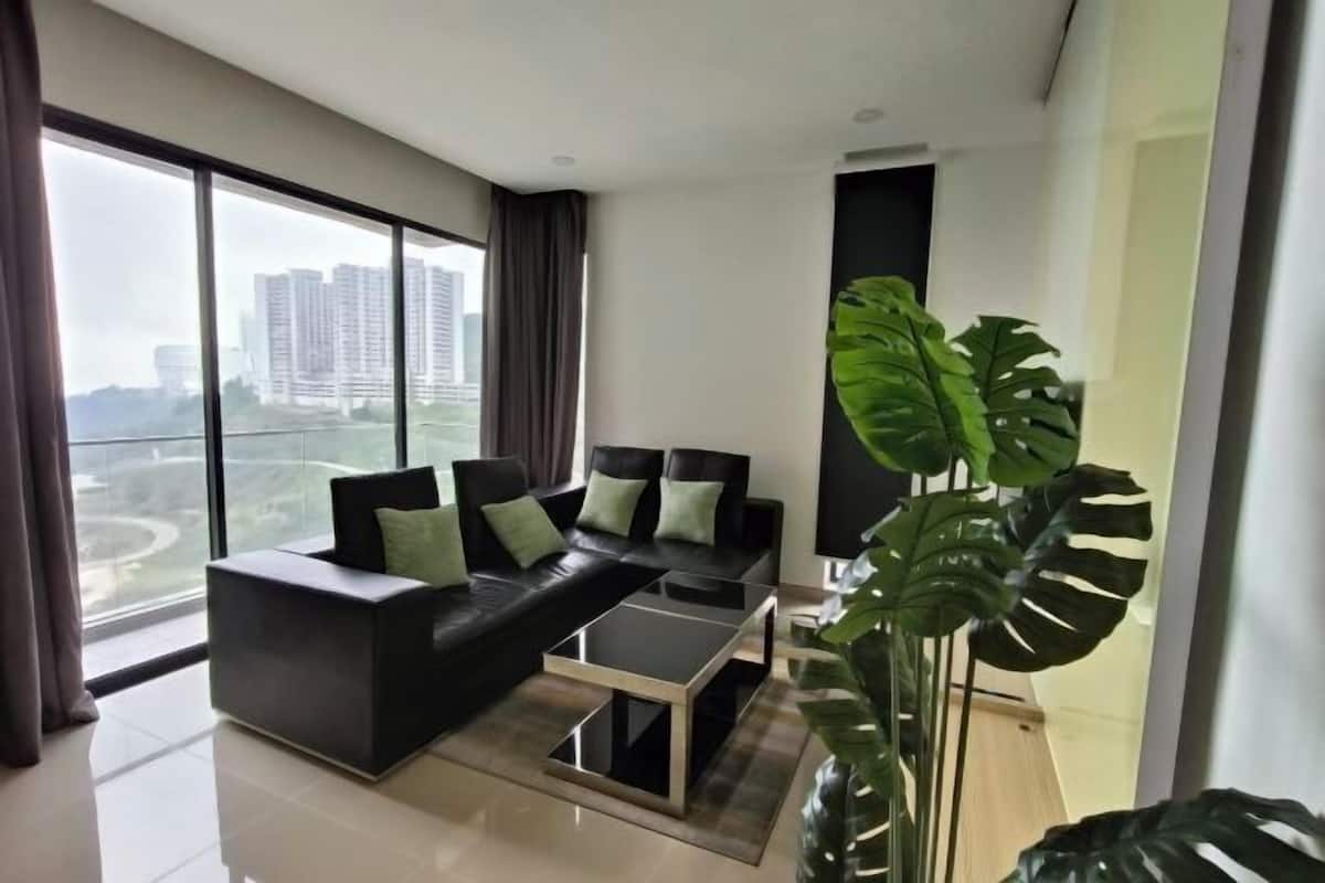 A modern living room with a black sofa, a glass coffee table, and a large plant.