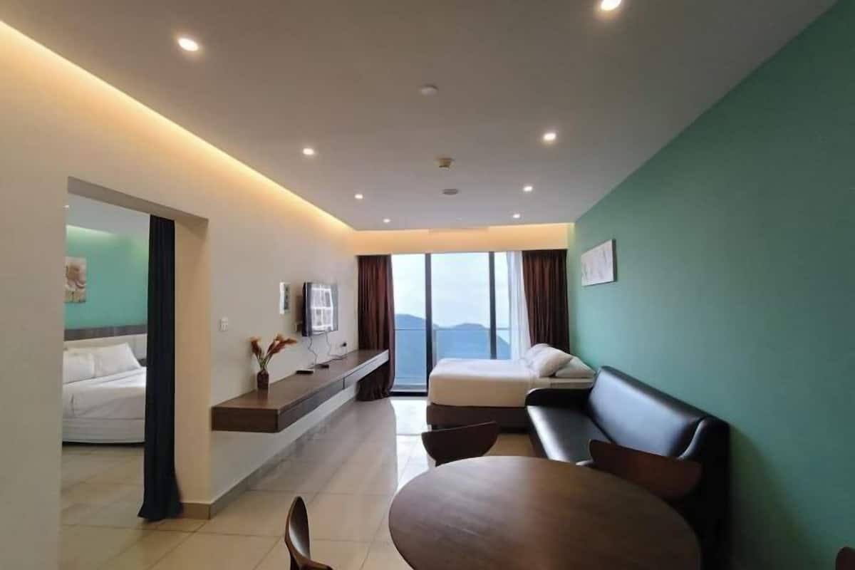 A modern hotel room with a bed, a sofa, a dining table, and a large window offering a view.