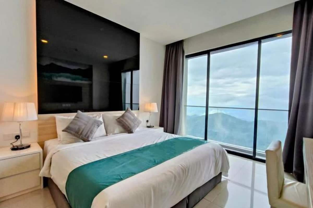 A modern hotel room with a large bed, two bedside tables, a view of the mountains through large windows, and a black accent wall.
