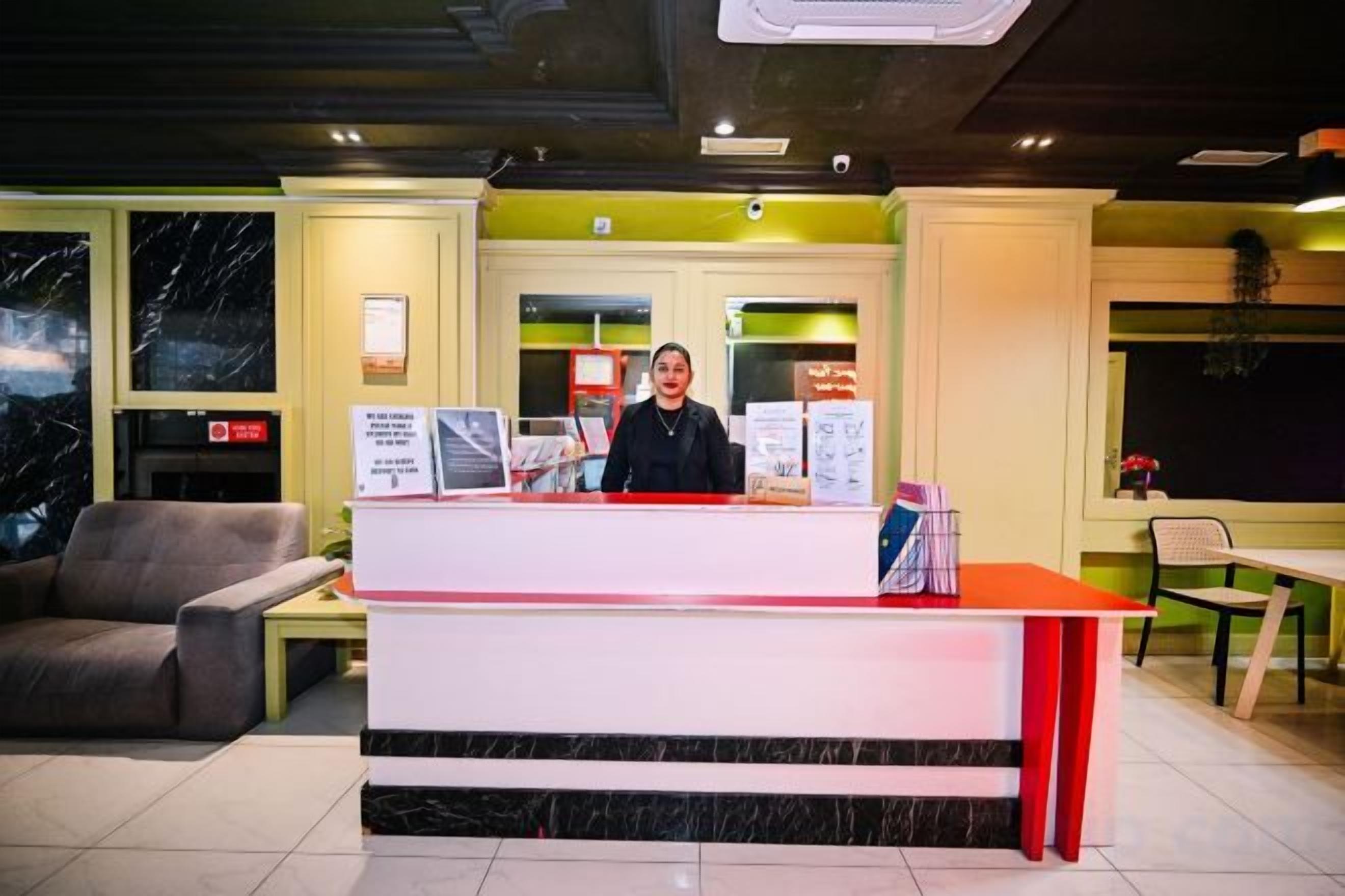 Un comptoir d’accueil avec une personne derrière, un espace détente avec un canapé et des fauteuils, et un panneau de signalisation indiquant la sortie, bien visible.