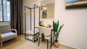 A room with a sofa, a desk with a chair, a hanging rack, a potted plant, and a TV mounted on the wall. - Kingston Hotel 1 @ Bukit Bintang (Kuala Lumpur)