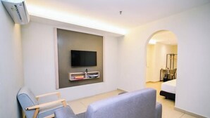 A modern hotel room with a flat-screen TV mounted on the wall, a grey sofa, a wooden chair, and a bed with a white mattress. - Kingston Hotel 1 @ Bukit Bintang (Kuala Lumpur)