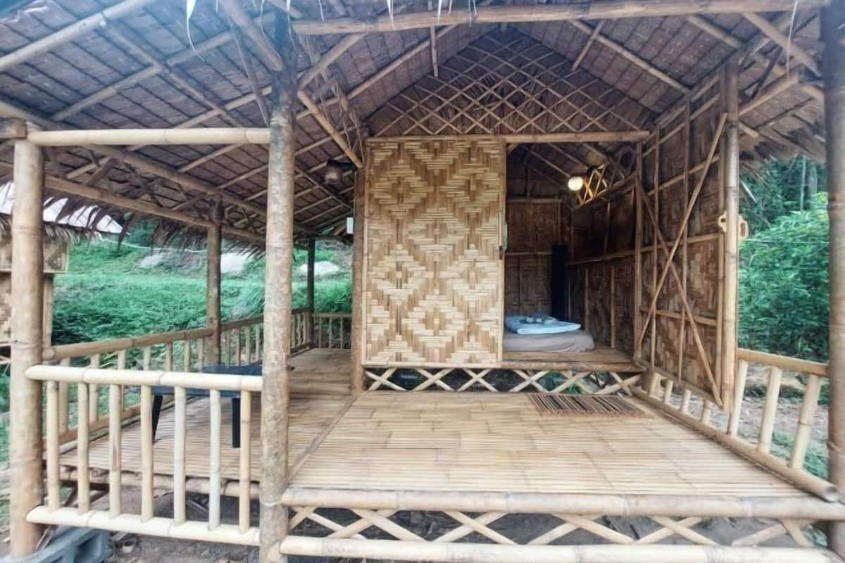 Estructura de bambú con un muro estampado, una pequeña zona de estar y una terraza de madera.
