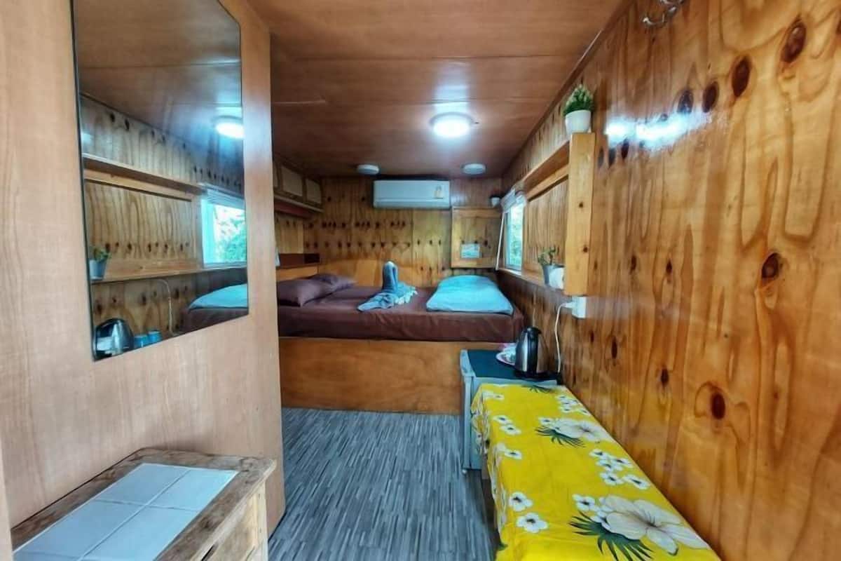 Una habitación pequeña con cama, una mesita, un banco y un espejo.