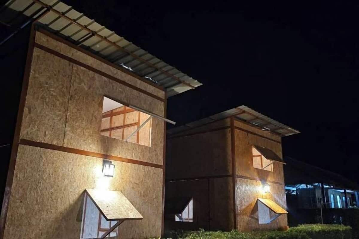 Dos edificios de madera con iluminación exterior, techo metálico y un ventanal pequeño.