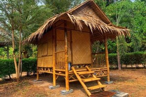 A bamboo hut with a thatched roof, surrounded by trees and a dry ground. - Samui Camping Farm (Koh Samui)