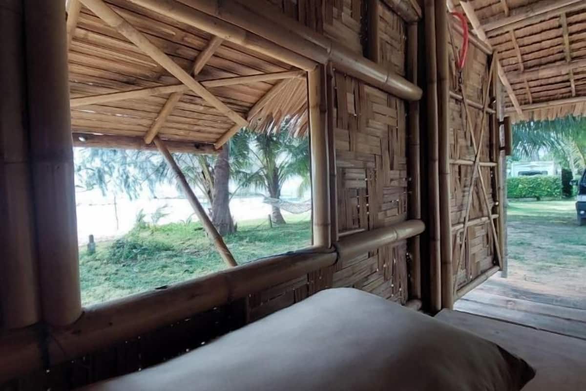 Una habitación con techo de paja, paredes de madera y ventana con vistas a un jardín.