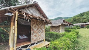 A bamboo structure with a thatched roof, a cushioned seating area, and a solar panel. - Samui Camping Farm (Koh Samui)