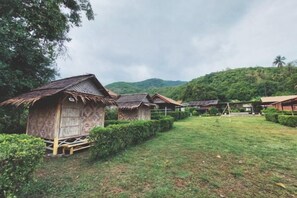Des huttes traditionnelles en bois, avec des toits de chaume, une zone herbeuse et une colline en arrière-plan.