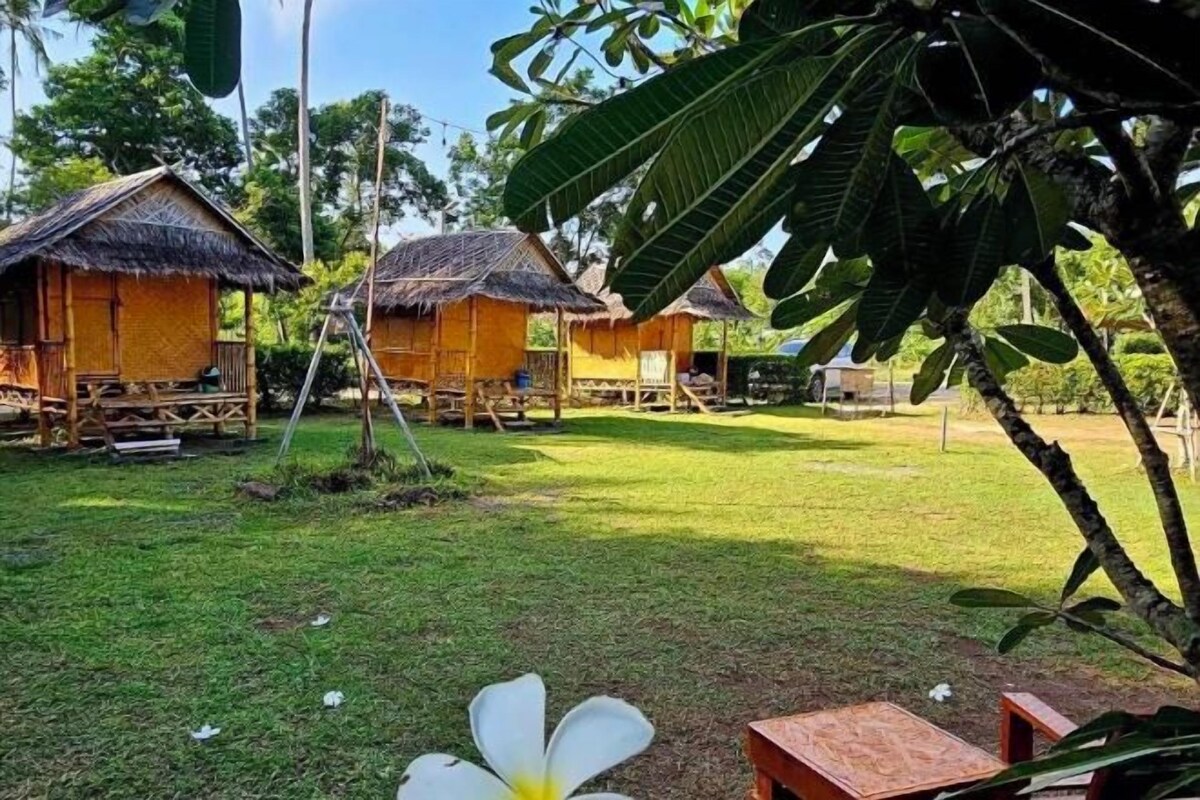 A series of thatched-roof huts with wooden decks, surrounded by lush greenery and a well-maintained lawn.