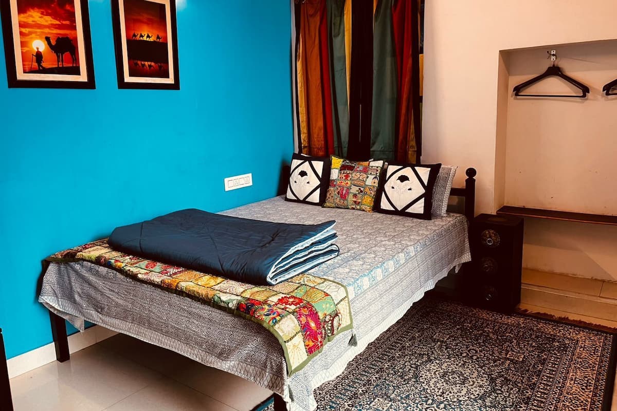 A bedroom with a bed, a blue wall, and a patterned rug.