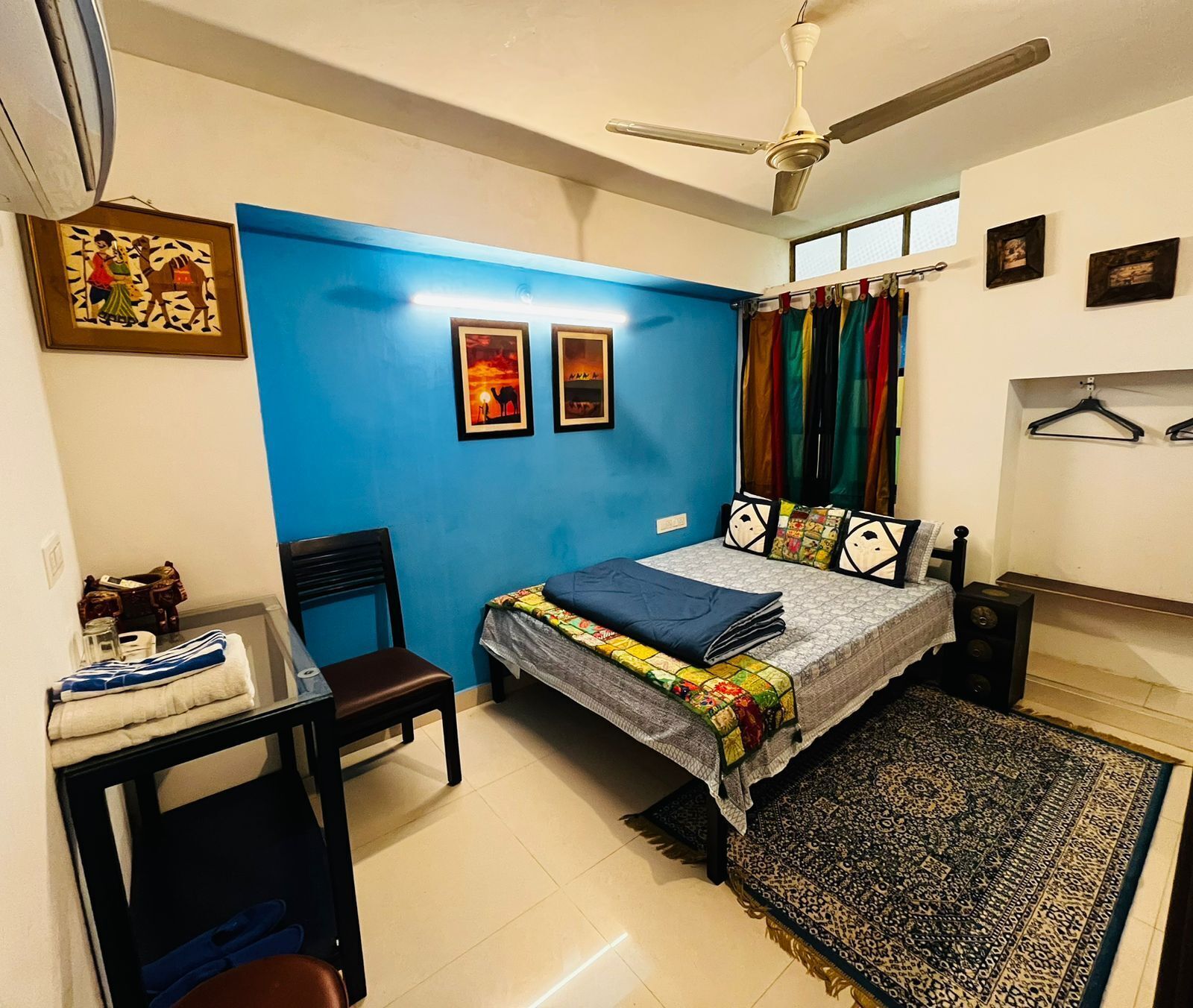 A bedroom with a bed, a desk, a chair, a ceiling fan, and a window with curtains.