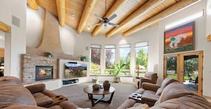 A spacious living room with a fireplace, comfortable seating, large windows, and a ceiling fan. - Corrales Family Estate Fire Pit & Playset (Corrales)