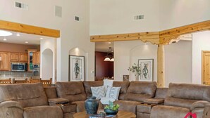 A spacious living area with a brown leather sectional sofa, a round coffee table, and a kitchen in the background. - Hacienda de Corrales – Irvie Signature Estate (Corrales)