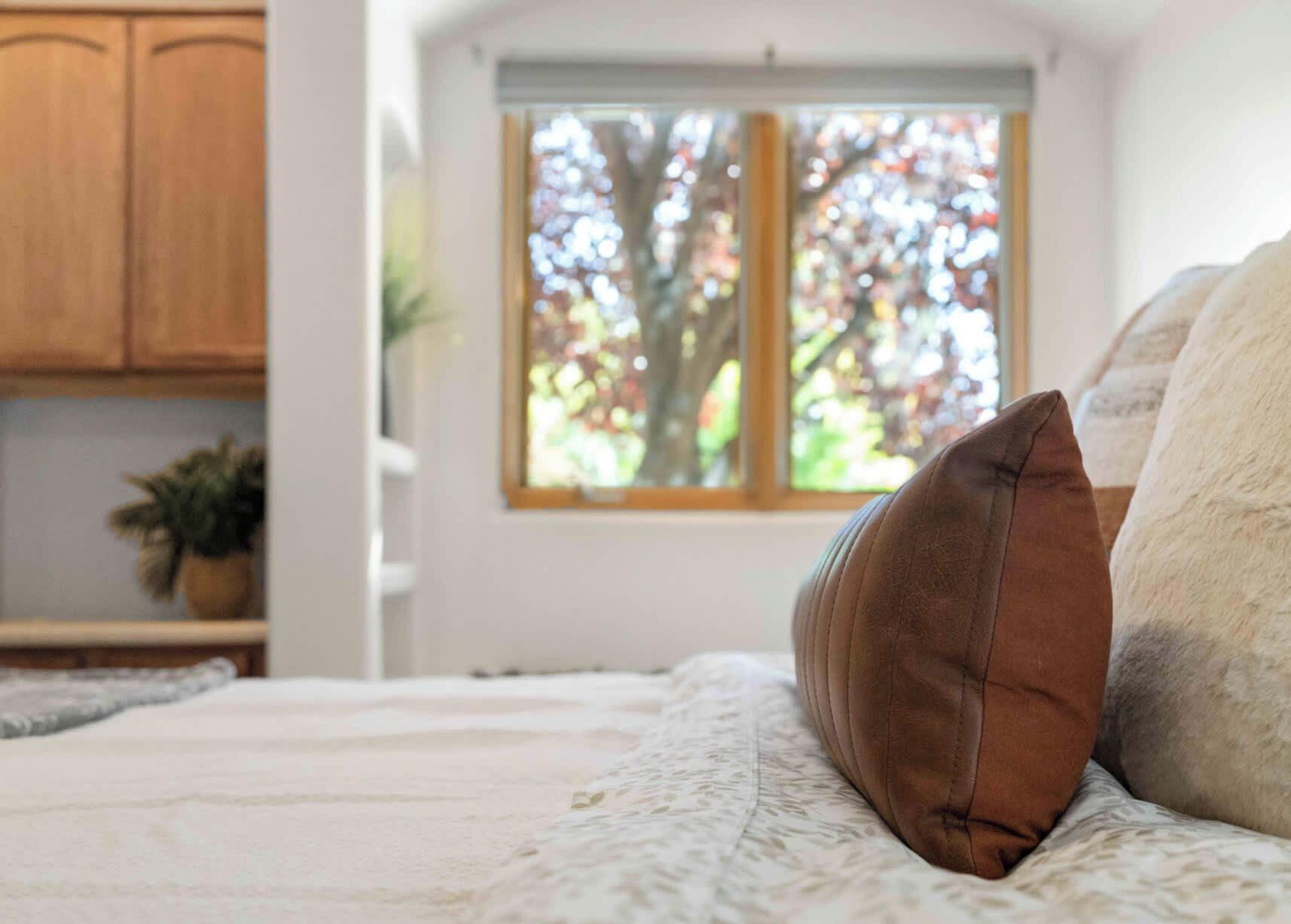 Une chambre à coucher avec un lit, une fenêtre donnant sur des arbres et des armoires en bois.