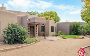A stucco building with a covered entryway and a small patio area. - Corrales Family Estate Fire Pit & Playset (Corrales)