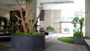 Un hall d’entrée avec un grand bac à plantes au centre, un comptoir d’accueil et une pancarte indiquant « Bienvenue chez vous ».