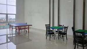 Une pièce spacieuse avec une table de ping-pong et quatre chaises, de grandes fenêtres offrant une belle vue et un aménagement propre et moderne.