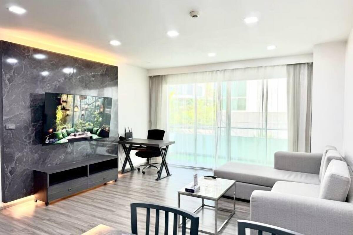 A modern living room with a flat-screen TV, a dining table, a sofa, and a large window.