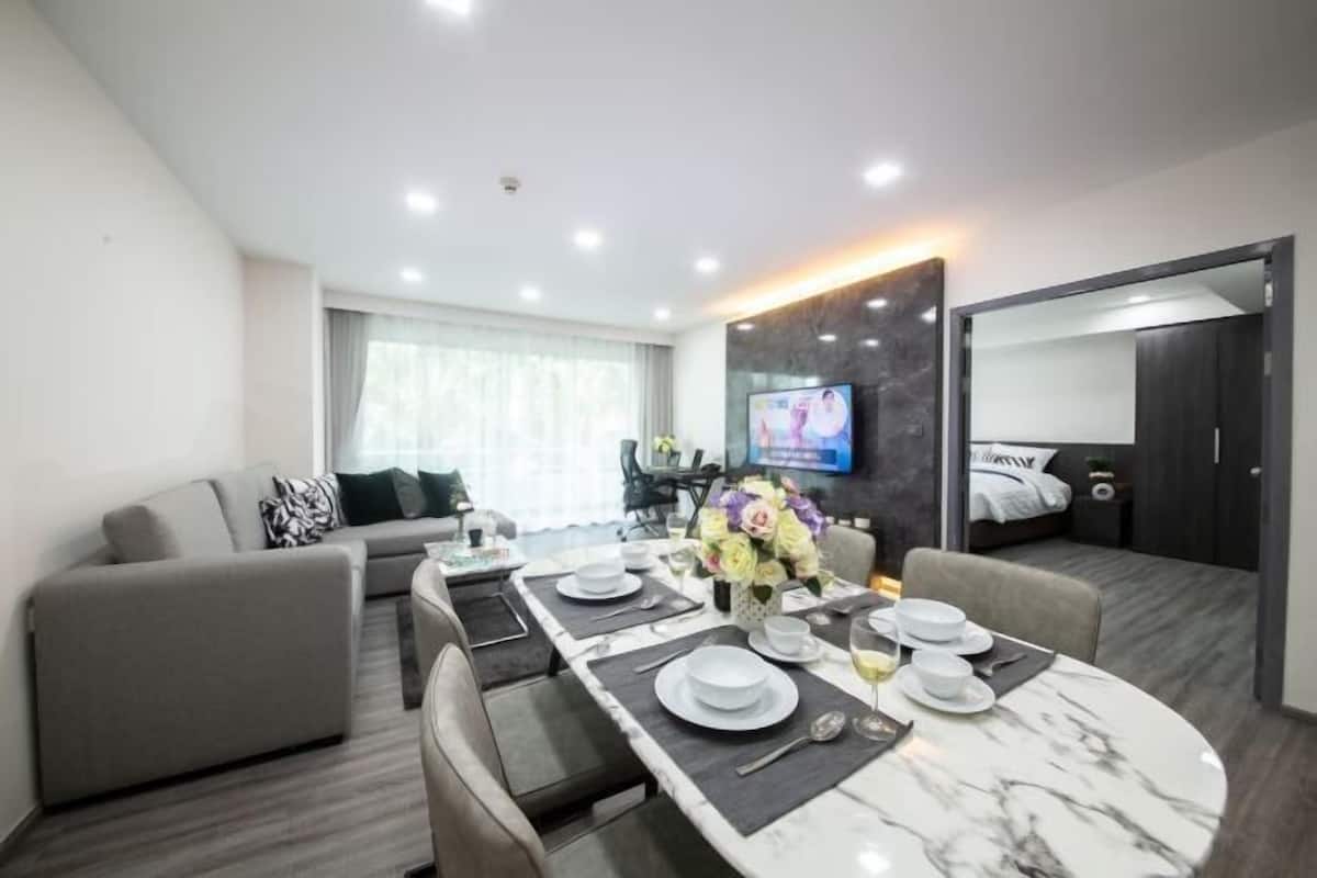 A modern hotel room with a dining area, a sofa, a TV, and a bed.