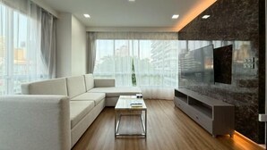 Una sala moderna con sofá, mesa de centro, televisor y vista a la ciudad.