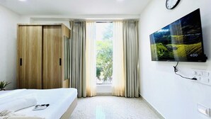 Una habitación de hotel con cama, armario, televisor montado en la pared y ventana con cortinas.