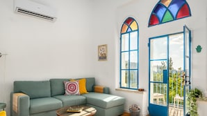 A living room with a green sofa, a small coffee table, and a large window with a blue door. - Jacuzzi Terrace Home by Sea N' Rent (Jerusalem)