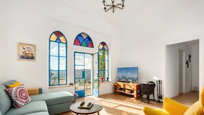 A living room with a sofa, armchair, and a coffee table. There are two windows with colorful stained glass, a fireplace, and a television. - Jacuzzi Terrace Home by Sea N' Rent (Jerusalem)