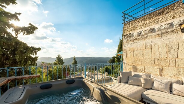 A hot tub with a view of mountains, a stone wall, and a white sofa with cushions. - Jacuzzi Terrace Home by Sea N' Rent (Jerusalem)