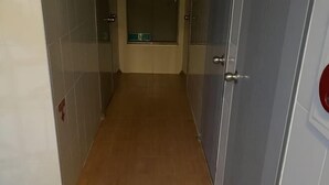 A narrow hallway with tiled walls and a wooden floor, leading to a door with a red handle. - GwangJu SunFlower Hostel (Gwangju)