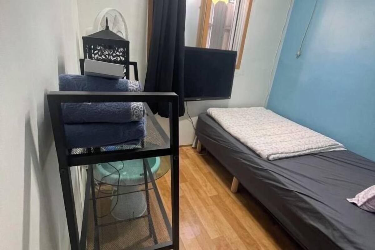 A small room with a bed, a desk with a chair, a TV, and a window with curtains.