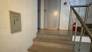 A staircase with a metal handrail, a fire alarm panel on the wall, and a door in the background. - GwangJu SunFlower Hostel (Gwangju)