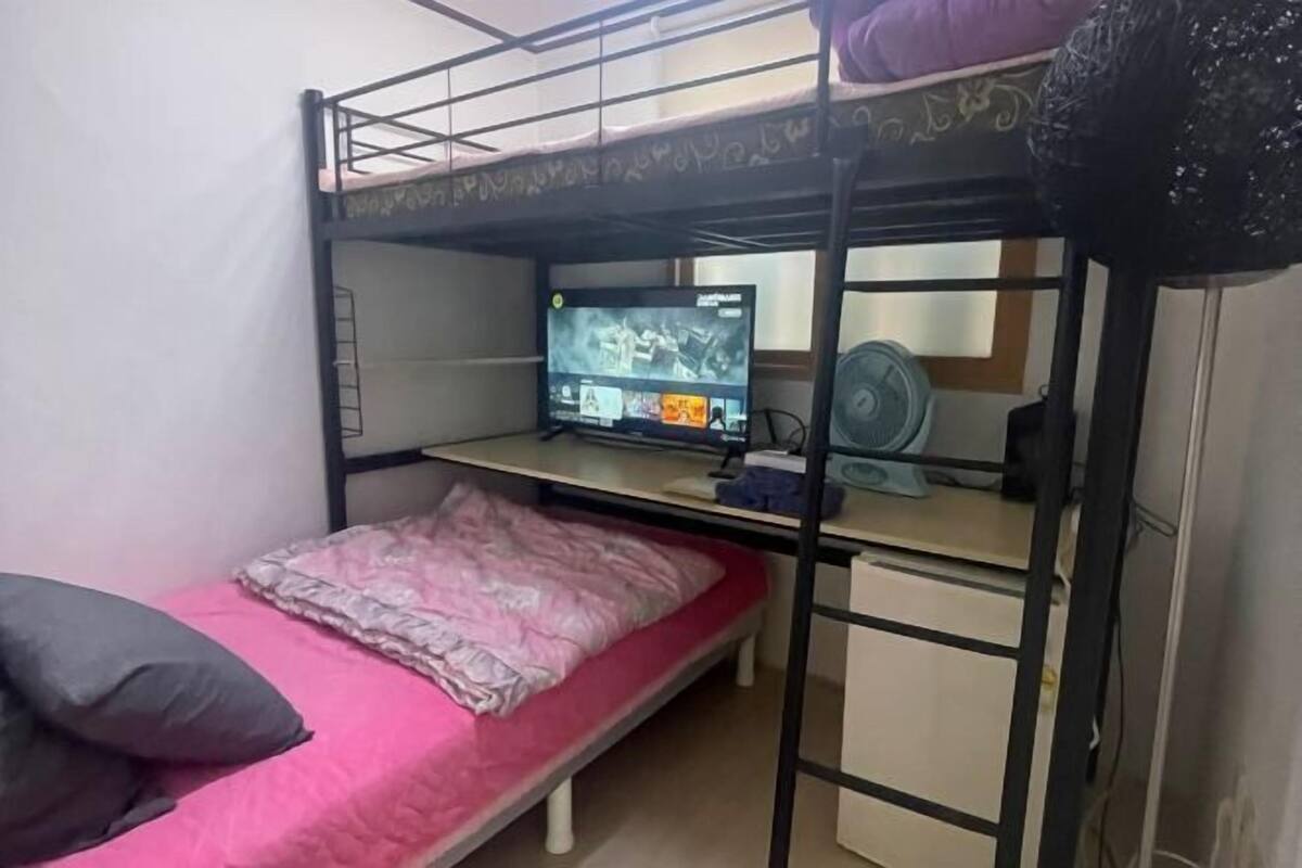 A bunk bed room with a desk, a computer, and a fan.